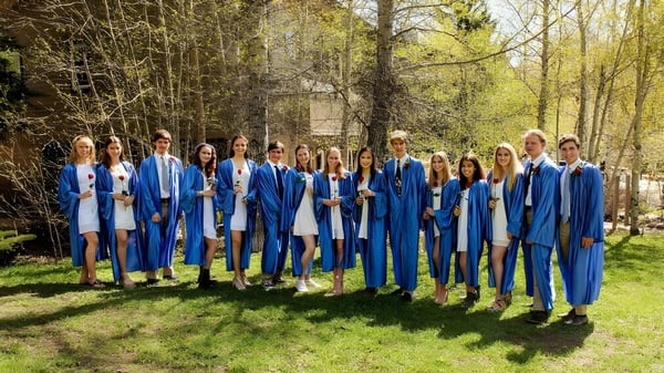 Los graduados de la Steamboat Mountain School están juntos en el bosque en togas azules.