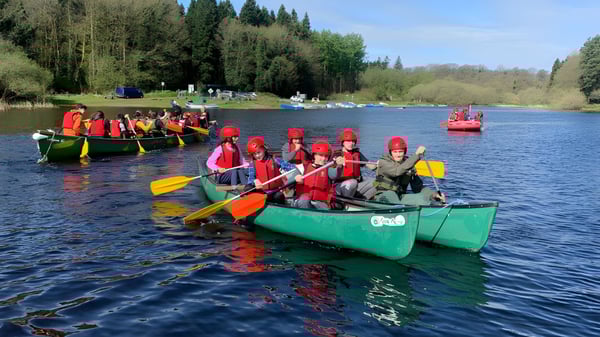 Alumnos de la Stepaside Educate Together Secondary School reman en canoas coloridas con chalecos salvavidas rojos en un lago.