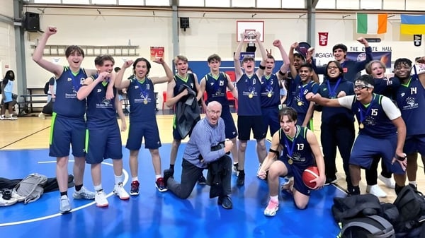 Un grupo de alumnas y alumnos de la Stepaside Educate Together Secondary School posan en el gimnasio con equipos deportivos y pancartas de fondo.