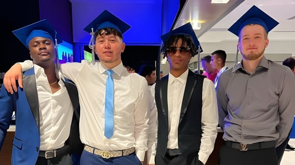 Un grupo de estudiantes de la Stephen Lewis Secondary School está junto en ropa de graduación frente a un fondo iluminado en azul y púrpura.