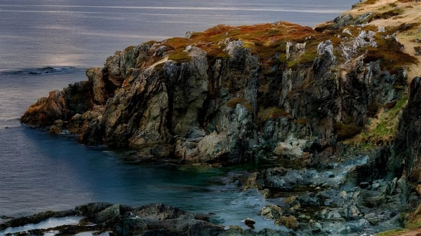 Acantilados rocosos con vegetación naranja-verde se elevan del agua turquesa cerca de la Stephenville High School.