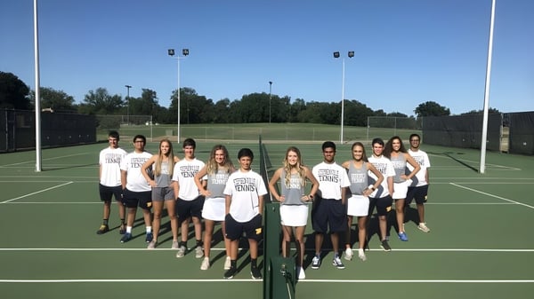 Un grupo de estudiantes de la Stephenville High School está juntos en una cancha de tenis frente a un campo de césped con árboles.