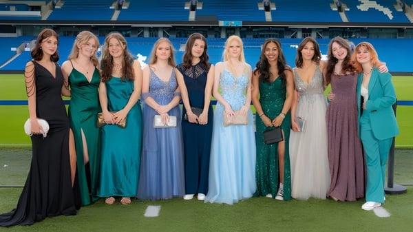 Un grupo de jóvenes estudiantes en vestidos de fiesta está de pie en el campo de deportes de Steyning Grammar School and Sixth Form con el estadio al fondo.