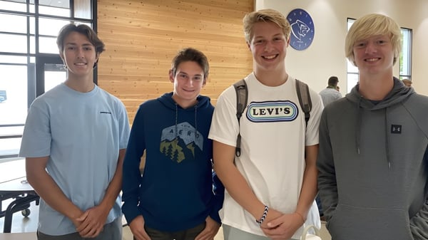 Cuatro estudiantes están juntos frente a una pared con el logo en el campus de la Stillwater Christian School.