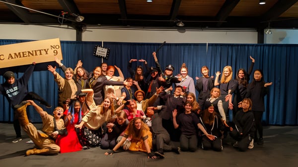Un gran grupo de estudiantes de la Stoneleigh-Burnham School posan en un escenario con fondo y iluminación.