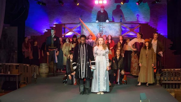 Estudiantes de la Stover School están en trajes llamativos en un escenario con iluminación colorida y un fondo decorativo.