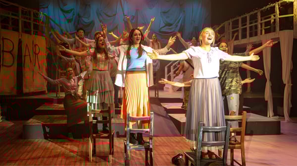 Estudiantes de la Stowe School realizan una animada actuación teatral en el escenario con coloridos trajes y fondos.