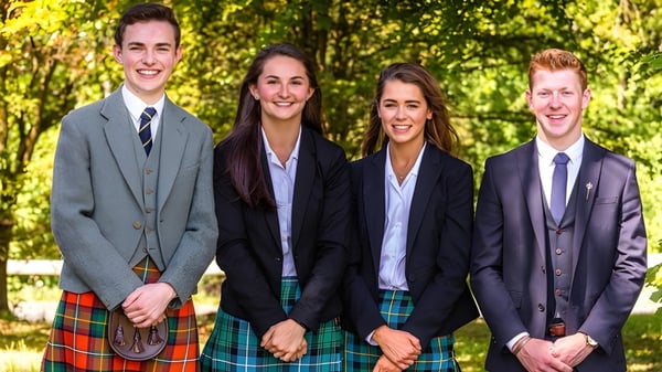Cuatro personas vestidas de manera formal están en el área exterior verde del campus del Stratford College.