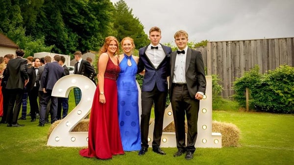 Un grupo de estudiantes del Stratford College está vestido de manera formal frente a la escultura del número 2 en un prado con árboles.