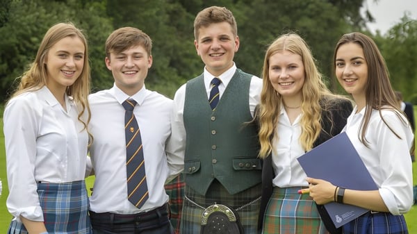 Un grupo de cinco estudiantes de la Strathallan School está juntos afuera en un área de césped con árboles.