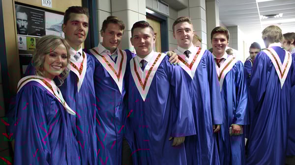 Estudiantes de la Strathmore High School en togas de graduación azules están de pie en el pasillo frente a una pizarra.