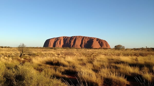 Una notable formación de arenisca roja se eleva bajo un cielo azul sobre un paisaje de hierba cerca del Stretton State College.