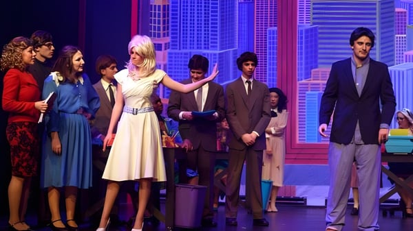 Un grupo de estudiantes está en el escenario de la Suffield Academy frente a un paisaje urbano como fondo.
