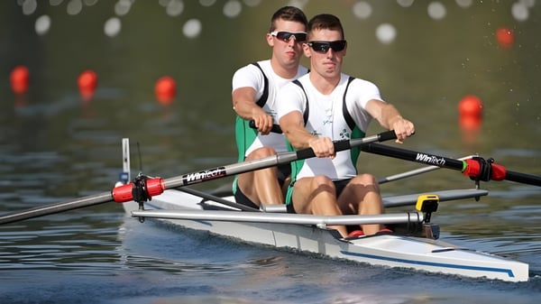Dos personas reman en un cuerpo de agua en medio de un paisaje verde en el campus del Summerhill College.
