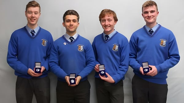 Cuatro estudiantes del Summerhill College llevan uniformes azules y sostienen pequeñas cajas con anillos frente a un fondo neutro.