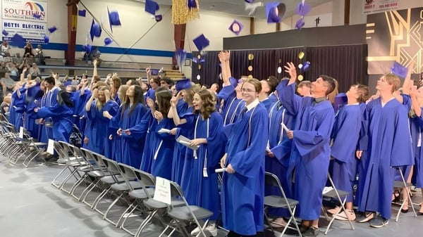 Un gran grupo de graduadas y graduados de la Summerland Secondary School lleva togas y birretes azules en la ceremonia de graduación.
