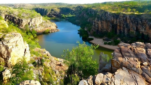 Un paisaje rocoso con acantilados empinados y un río turquesa fluye a través de un valle verde en el terreno de la Sunshine Beach State High School.