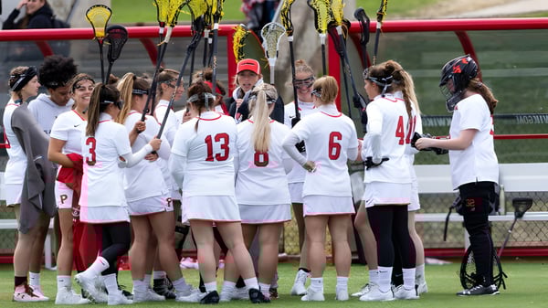 Un grupo de jóvenes atletas está en el campo deportivo de la SUNY Plattsburgh con camisetas blancas con números.