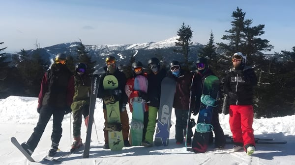 Estudiantes de la SUNY Plattsburgh están en colorida ropa de esquí frente a un paisaje montañoso nevado.
