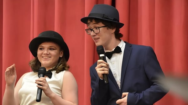 Dos personas están en el escenario de la Sutton Park School y hablan con micrófonos frente a una cortina roja.
