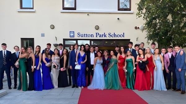 Estudiantes de la Sutton Park School en Dublín están en elegante vestimenta de noche frente al edificio escolar en una alfombra roja.