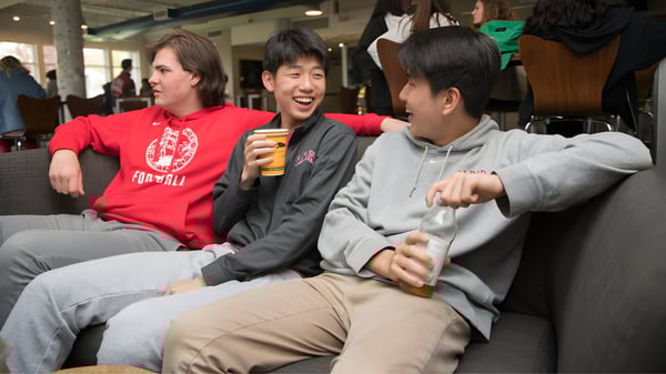 Tres estudiantes se sientan juntos en un área pública del campus de Tabor Academy y conversan.
