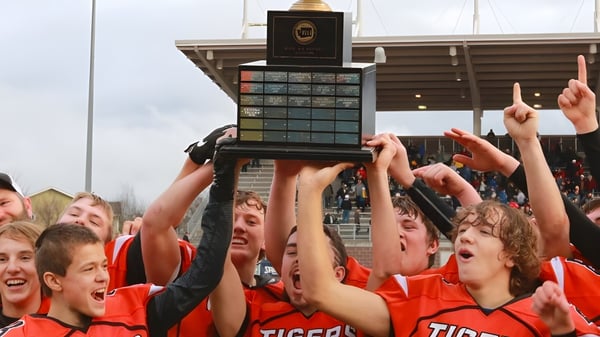 Un grupo de estudiantes de Tacoma Public Schools celebra la victoria de un trofeo frente a un edificio tipo estadio.