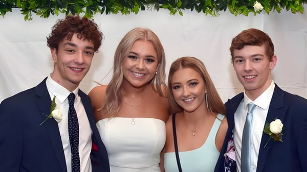 Cuatro estudiantes del Taieri College posan juntos frente a un fondo floral en un marco formal.