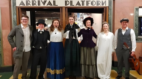Un grupo de estudiantes del Taieri College está frente al cartel 'Plataforma de llegada' en una estación de tren.