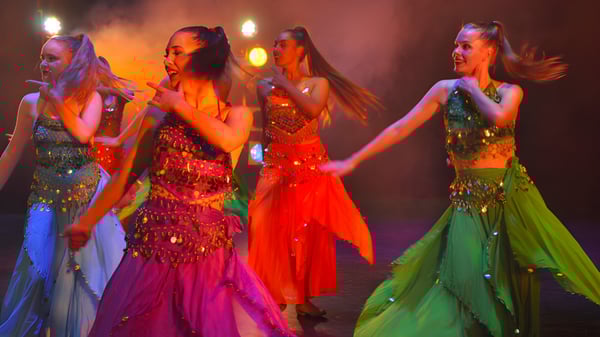 Cuatro alumnas de la Takapuna Grammar School realizan una actuación en un escenario con iluminación dramática vestidas con trajes coloridos.