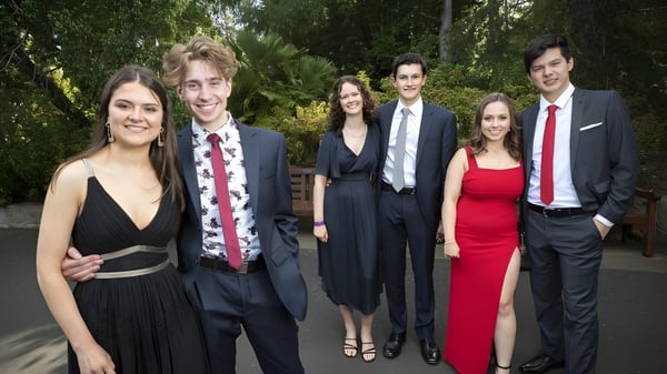 Un grupo de personas bien vestidas posan juntos en un área exterior verde de la Taroona High School.