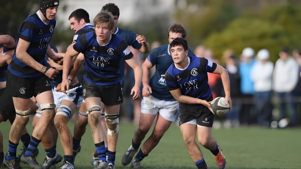Un grupo de jóvenes jugadores de rugby en camisetas azules juega en el campo deportivo de la Taroona High School.