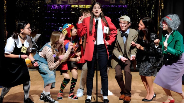Un grupo de estudiantes de TASIS The American International School in England está en un escenario frente a un fondo iluminado con neón.