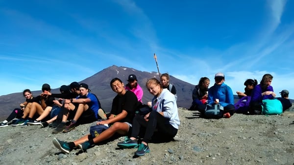 Un grupo de estudiantes de la Taumarunui High School está sentado frente a una montaña nevada bajo un cielo azul.