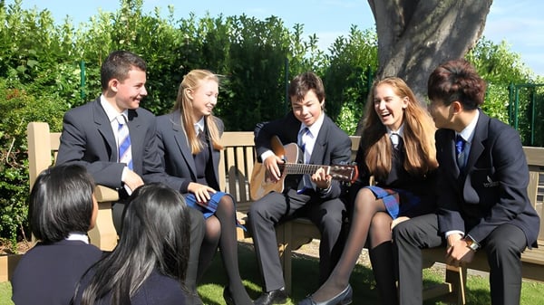 Estudiantes de Taunton School International conversan con ropa formal al aire libre con vegetación verde de fondo.