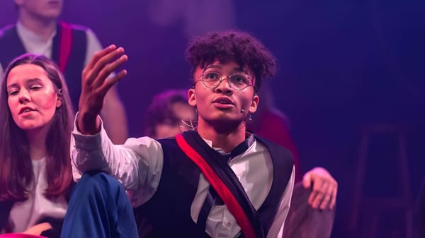 Un estudiante de Taunton School International está de pie en un escenario y gesticula expresivamente durante una actuación.