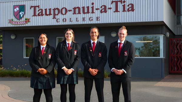 Cuatro personas en ropa formal están frente al edificio del Taupo-nui-a-Tia College.