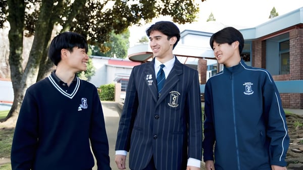 Tres estudiantes en uniforme escolar están juntos en el patio del Tauranga Boy's College.
