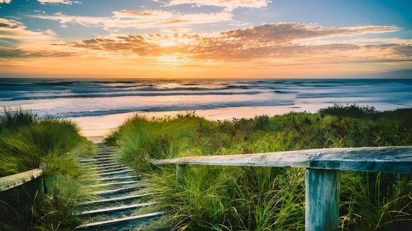 Una playa con una escalera de madera hacia el mar al atardecer muestra una escena cerca del Tauranga Boy's College.