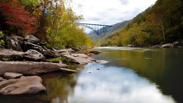 Un río tranquilo fluye a través de un paisaje otoñal con un alto puente de fondo en el terreno de la Teays Valley Christian School.