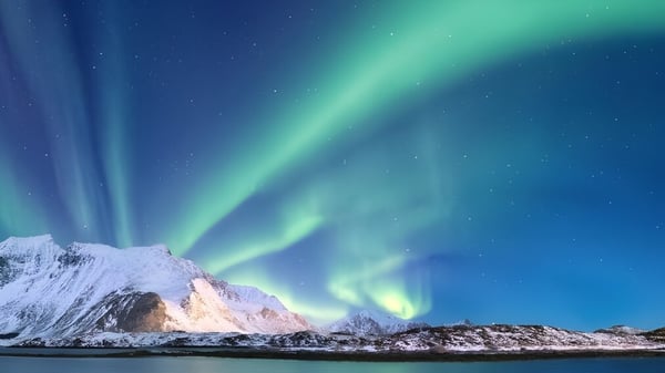 Montañas cubiertas de nieve con la aurora boreal verde y azul en el cielo nocturno cerca de la Tecumseh Vista Academy.