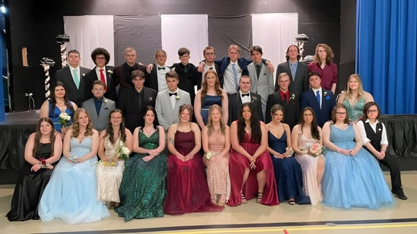 Un gran grupo de alumnas y alumnos de la Templeton Academy está en un escenario frente a un fondo negro y cortinas azules.