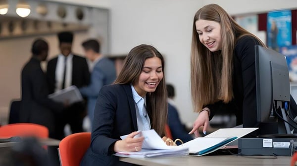Dos estudiantes de Tettenhall College discuten juntas documentos de negocios en una oficina profesional.