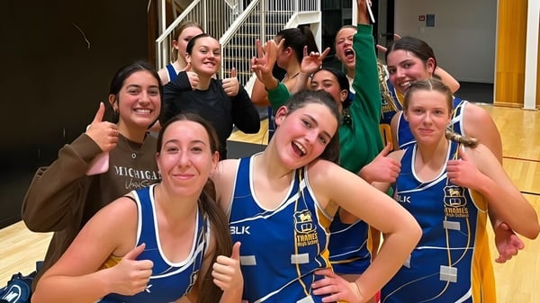 Un grupo de estudiantes de la Thames High School posan en uniformes deportivos azules en un gimnasio.