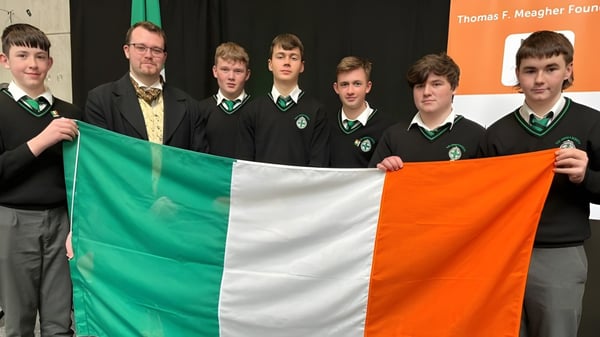 Estudiantes de The Abbey School en uniforme sostienen una bandera irlandesa frente a un banner de la Thomas F. Meagher Foundation.