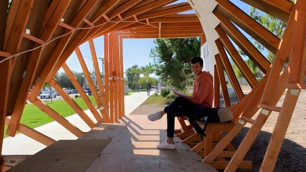 Una persona está sentada en un banco en el sendero de madera con un patrón geométrico en el campus de The Academy MiraCosta.