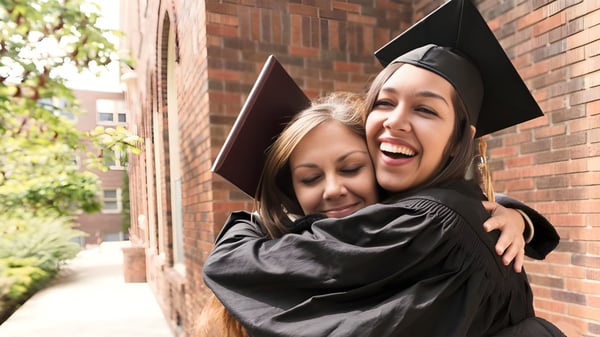 Dos estudiantes de The Barnes Academy se abrazan riendo frente a un edificio de ladrillo durante la ceremonia de graduación.