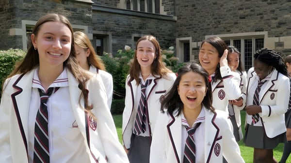 Un grupo de alumnas sonrientes de The Bishop Strachan School está frente a un edificio de piedra con ventanas de arco.