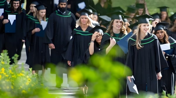 Las graduadas y graduados de The Bishop Strachan School caminan en togas por un camino flanqueado de naturaleza verde.