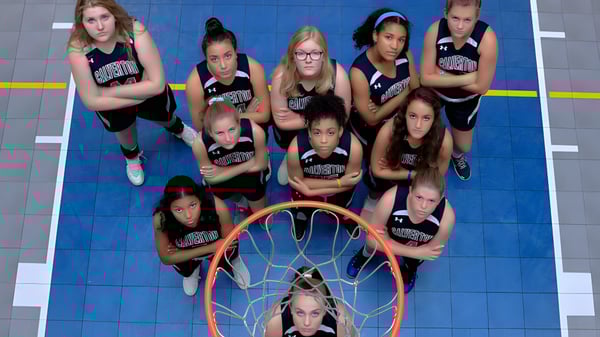 Un grupo de jóvenes jugadoras de baloncesto está en la cancha de baloncesto de The Calverton School con una canasta en primer plano.